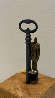 Mixed Media Objekte, Kunst, Eisenschlüssel mit Keramikfigur auf Holzsockel. Die kleinen gebrannten Figuren schimmern bronzefarbig.