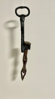 Mixed Media Objekte, Kunst, Eisenschlüssel mit Keramikfigur auf Holzsockel. Die kleinen gebrannten Figuren schimmern bronzefarbig.